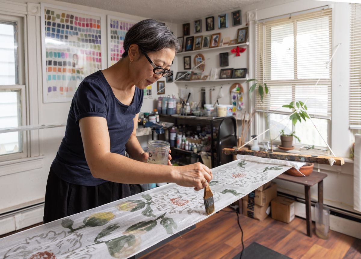 Textile artist Yuh Okano paints a long length of silk in her studio.